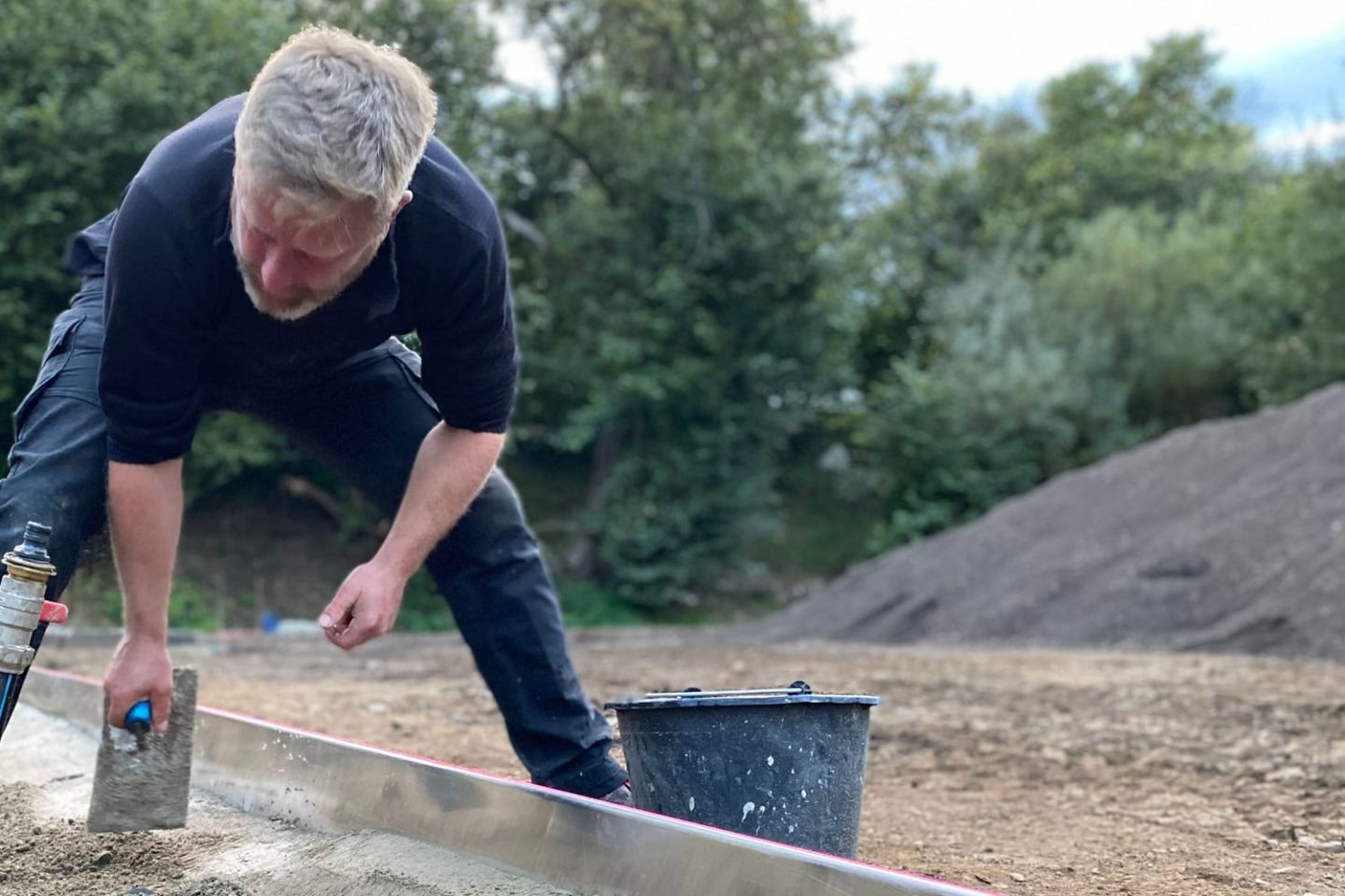 Handwerker zieht frischen Mörtel an einer Aluminiumlatte ab, daneben ein Mörtelkübel